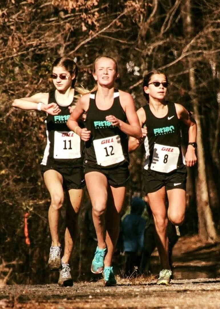 Three student athletes running together through woods, two are wearing sunglasses